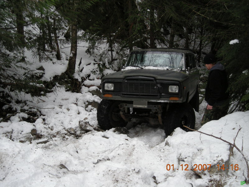 Lifted Jeep Cherokee driving through snow in a forest.