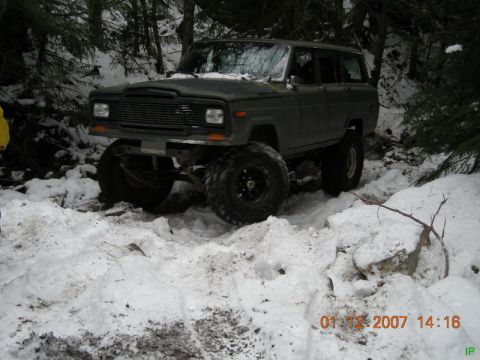 Lifted dark green Jeep Cherokee on a snowy forest trail.