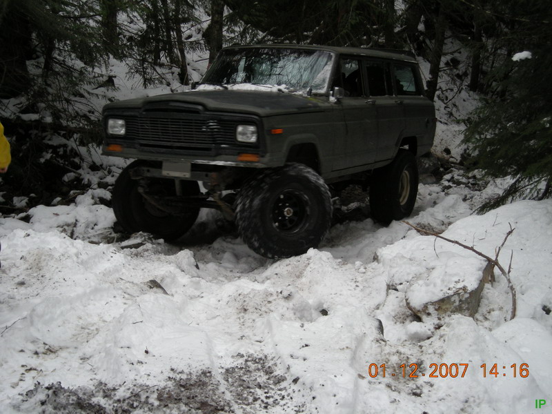 Lifted dark green Jeep Cherokee on a snowy forest trail.