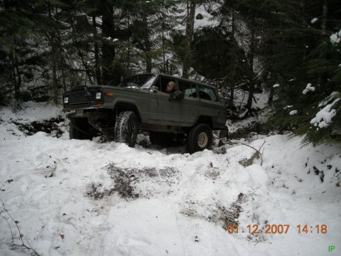 Dark green Jeep Cherokee navigating a snowy forest trail.