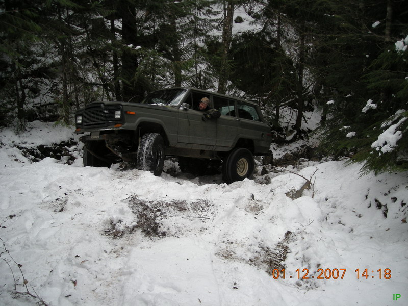 Dark green Jeep Cherokee navigating a snowy forest trail.