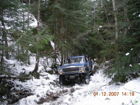 Blue 1980s Ford pickup truck on a snowy, wooded trail.