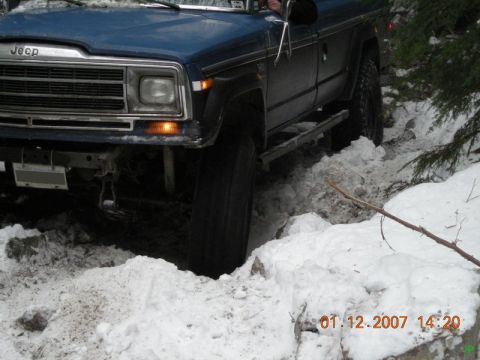 Blue Jeep SUV on a snowy off-road trail, front view.