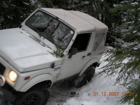 White soft-top SUV driving through snow in a forest.