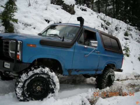 Blue Ford Bronco with snorkel and large tires driving in snow.
