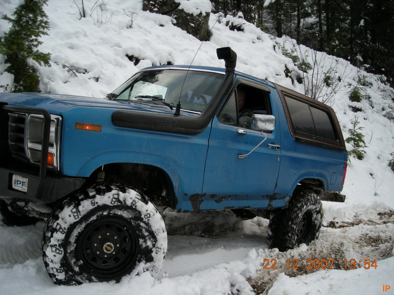 Blue Ford Bronco with snorkel and large tires driving in snow.