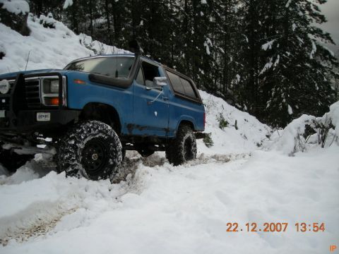 Blue lifted Ford Bronco with snorkel and off-road tires driving in snow.