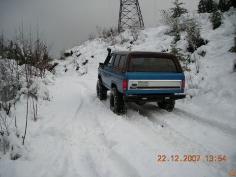 1985 Ford Bronco driving on a snowy road, rear view.