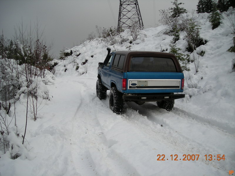 1985 Ford Bronco driving on a snowy road, rear view.