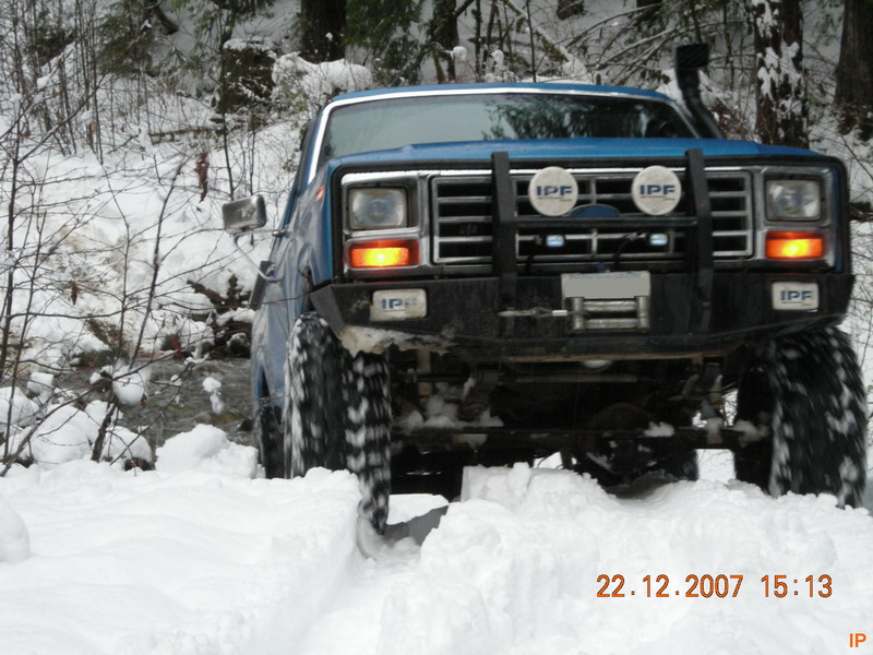Blue Ford Bronco driving through snow on a wooded trail.