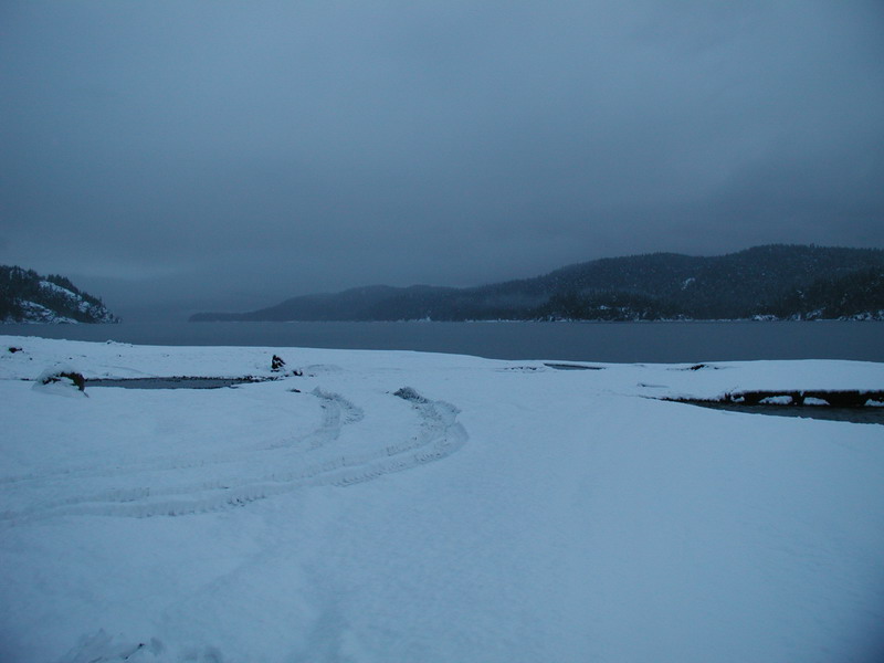 Snowy landscape with tire tracks and water.