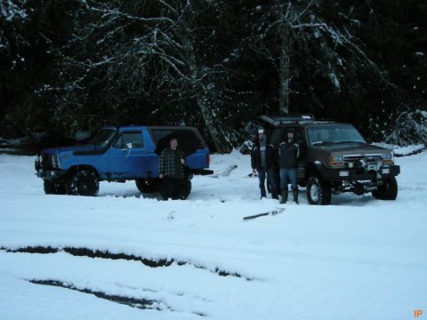 Two SUVs in the snow with people standing around them.