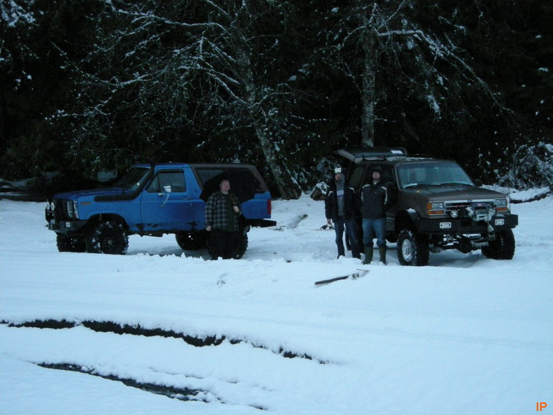 Two SUVs in the snow with people standing around them.