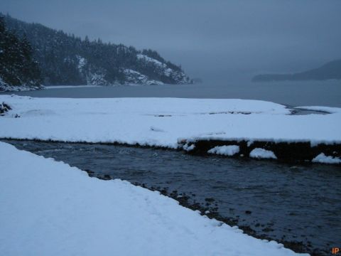 Snow-covered landscape with a stream flowing into a bay.