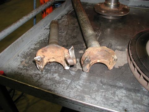 Two damaged CV axle shafts on a workbench.