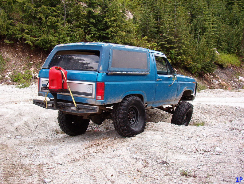 Lifted blue Ford Bronco with jerrycan on rear bumper, parked on a dirt road.