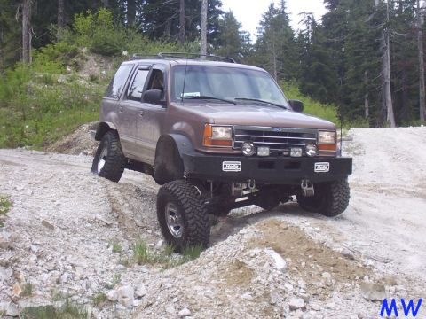 Lifted brown Ford Explorer off-roading on a rocky hill.