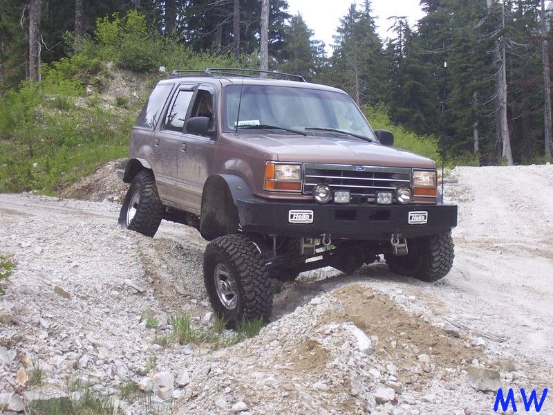 Lifted brown Ford Explorer off-roading on a rocky hill.