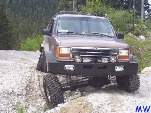 Lifted brown Ford Explorer off-roading with front passenger tire in the air.