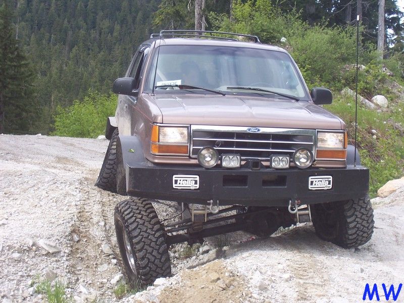 Lifted brown Ford Explorer off-roading with front passenger tire in the air.