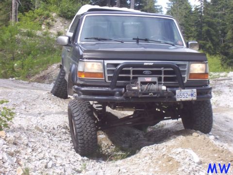 Dark Ford Bronco with winch and off-road tires on a rocky trail.