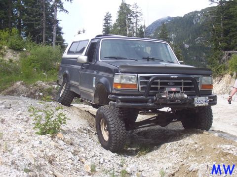 Lifted Ford Bronco with winch on a rocky off-road trail.