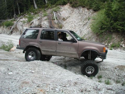 Lifted brown SUV on a rocky off-road trail, front passenger wheel high.