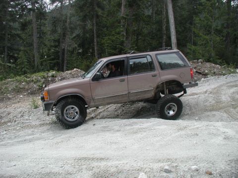 Lifted tan SUV driving off-road on a dirt path.