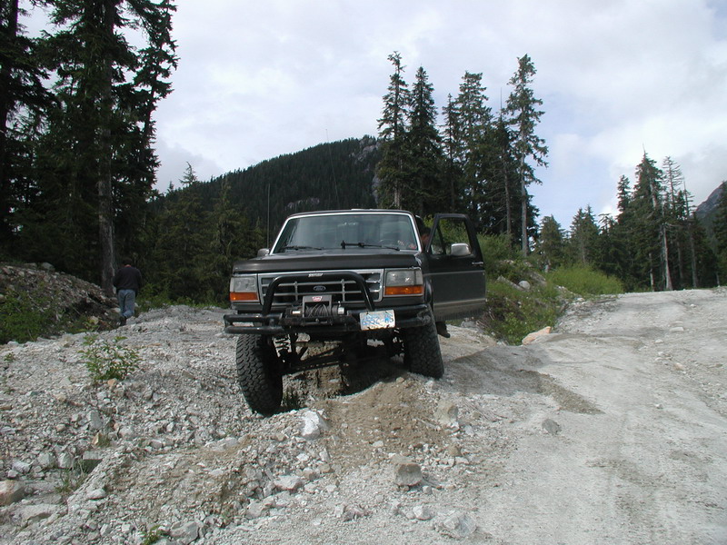 Dark Ford Bronco on a rocky off-road trail with winch and open door.