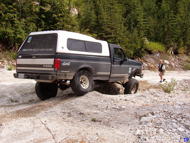 Lifted Ford pickup truck with white camper shell on a dirt road, man walking behind.