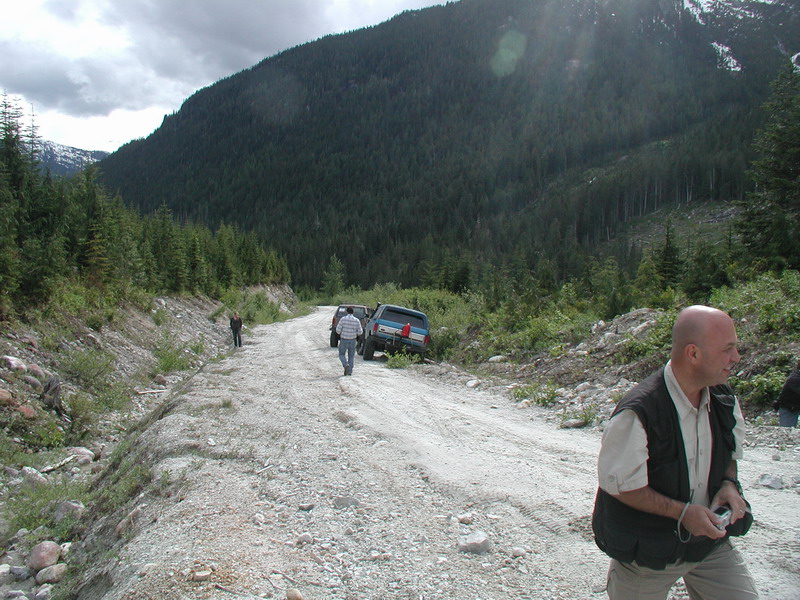 Two SUVs on a gravel road in a mountainous, forested area.