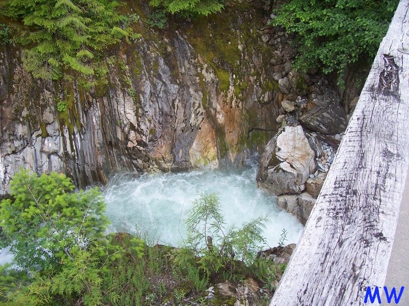River flowing through a rocky gorge with trees and a wooden railing.