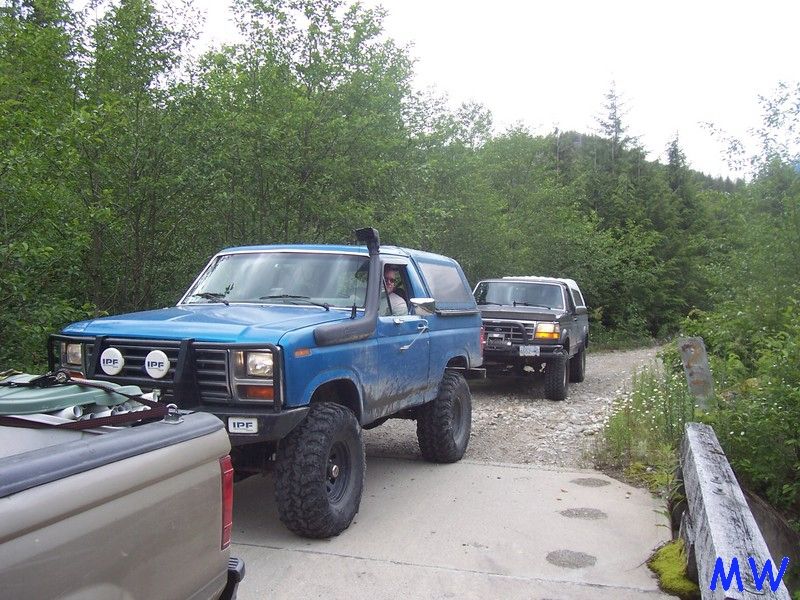 Blue Ford Bronco with snorkel and aftermarket bumper on a dirt road.