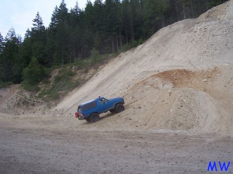 Blue 1980s Ford Bronco SUV driving up a steep, sandy hill.