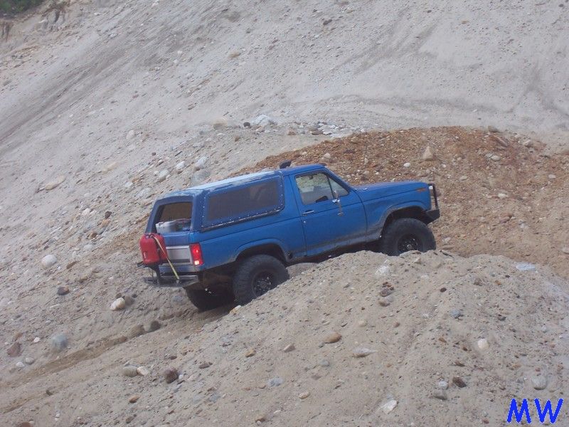 Blue Ford Bronco off-roading on a sandy hill, rear-side view.