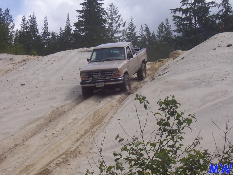 Tan Ford pickup truck driving up a sandy hill.