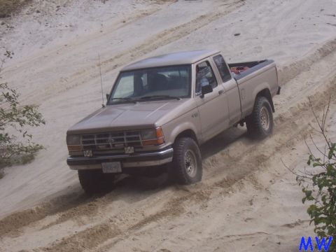 Tan Ford pickup truck driving up a sandy hill, kicking up dust.