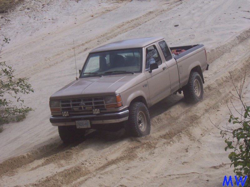 Tan Ford pickup truck driving up a sandy hill, kicking up dust.