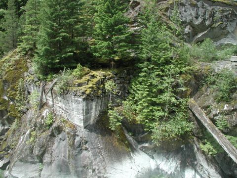 Concrete structure on a cliff face with trees and a wooden beam.