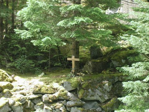 Wooden cross with a sign in a forest clearing.