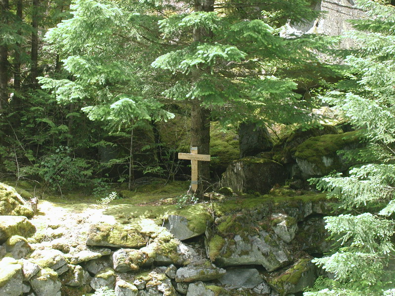 Wooden cross with a sign in a forest clearing.