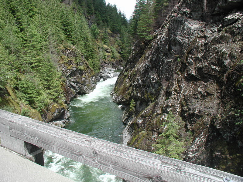 River flowing through a rocky canyon with trees and a wooden railing in the foreground.