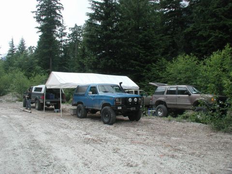 Blue Ford Bronco and brown Ford Explorer parked under a canopy in a forest.
