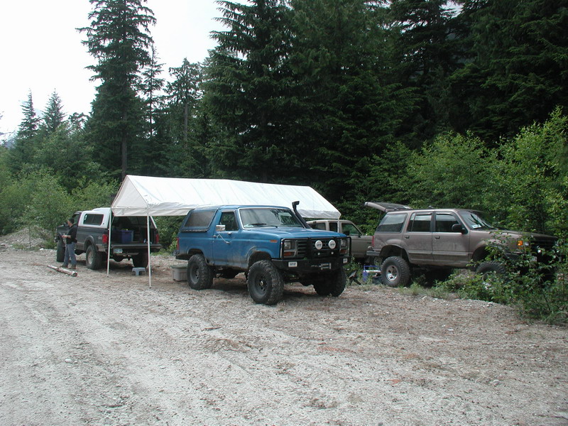 Blue Ford Bronco and brown Ford Explorer parked under a canopy in a forest.