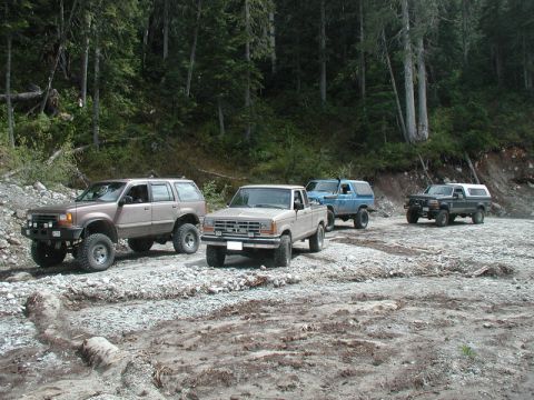 Four off-road vehicles on a rocky trail in a forest.