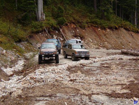 Four-wheel drive vehicles on a rough dirt road in a wooded mountain area.