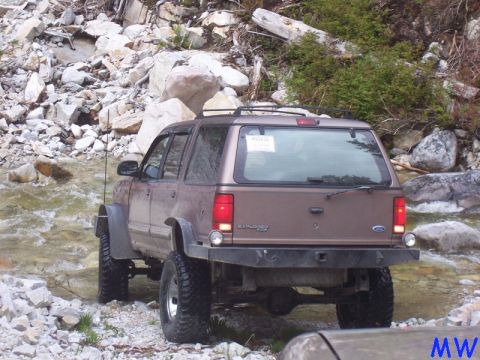 Lifted brown Ford Explorer driving through a rocky stream.