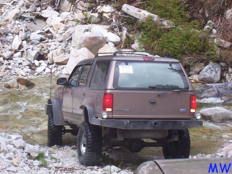 Lifted brown Ford Explorer driving through a rocky stream.