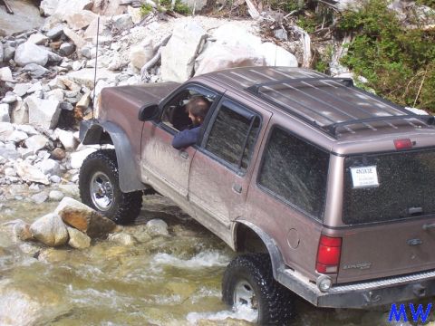 Brown Ford Explorer off-roading through a rocky stream.