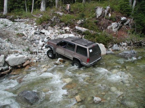 Lifted brown SUV driving through a rocky stream.